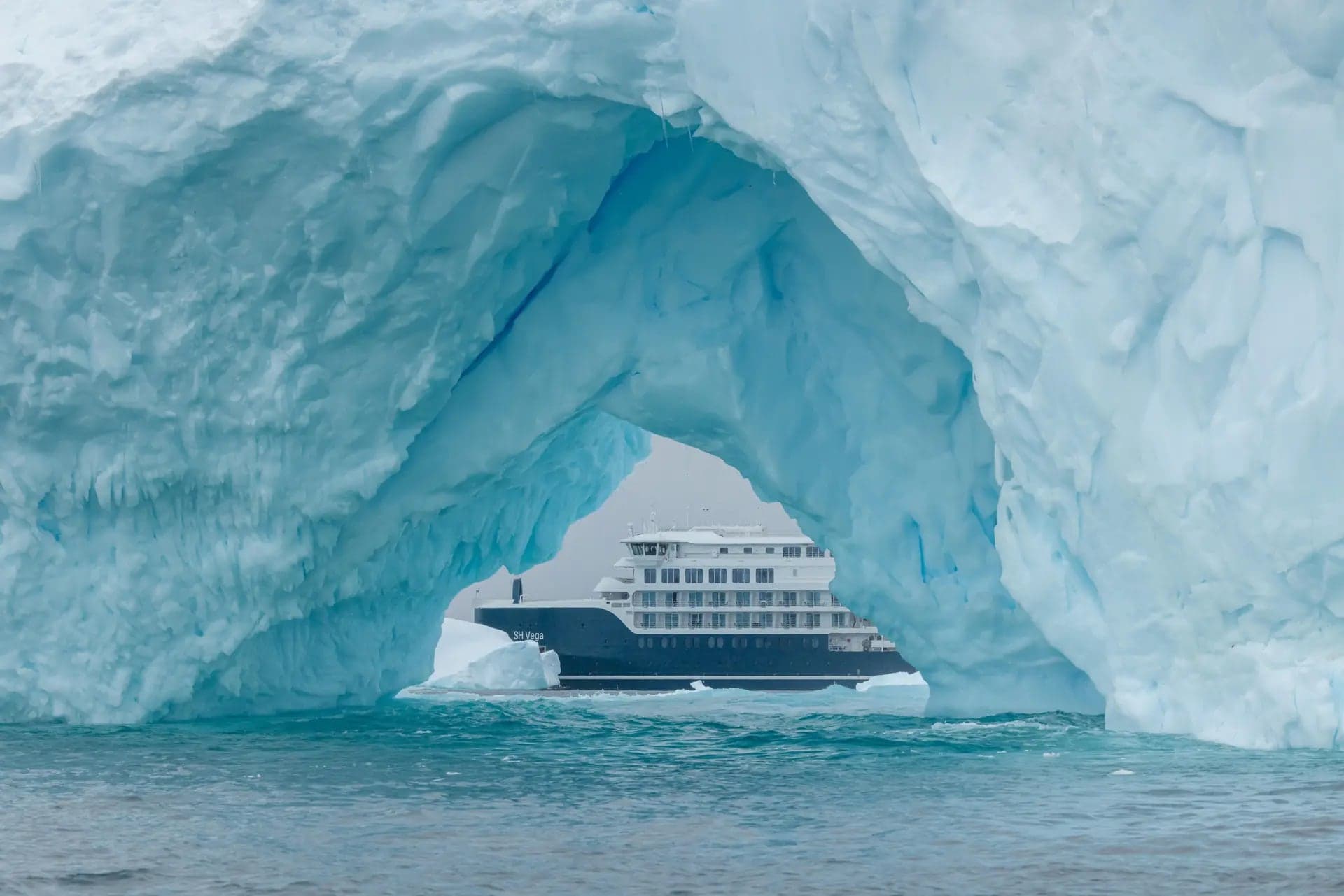 The expedition ship framed in a natural iceberg arch, Antarctic Peninsula